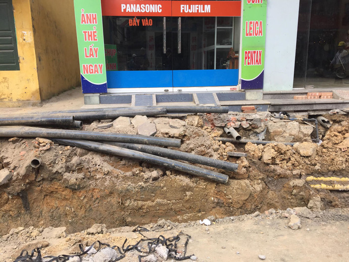 Người dân phải đi lại qua những chiếc cầu gỗ bắc tạm để vượt qua khu vực thi công hệ thống thoát nước hai ven đường với chiều rộng gần 2 mét.