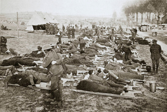 Những người lính bị thương nằm trên cáng tại một khu đất rộng được đồng đội và nhân viên y tế điều trị và chăm sóc.