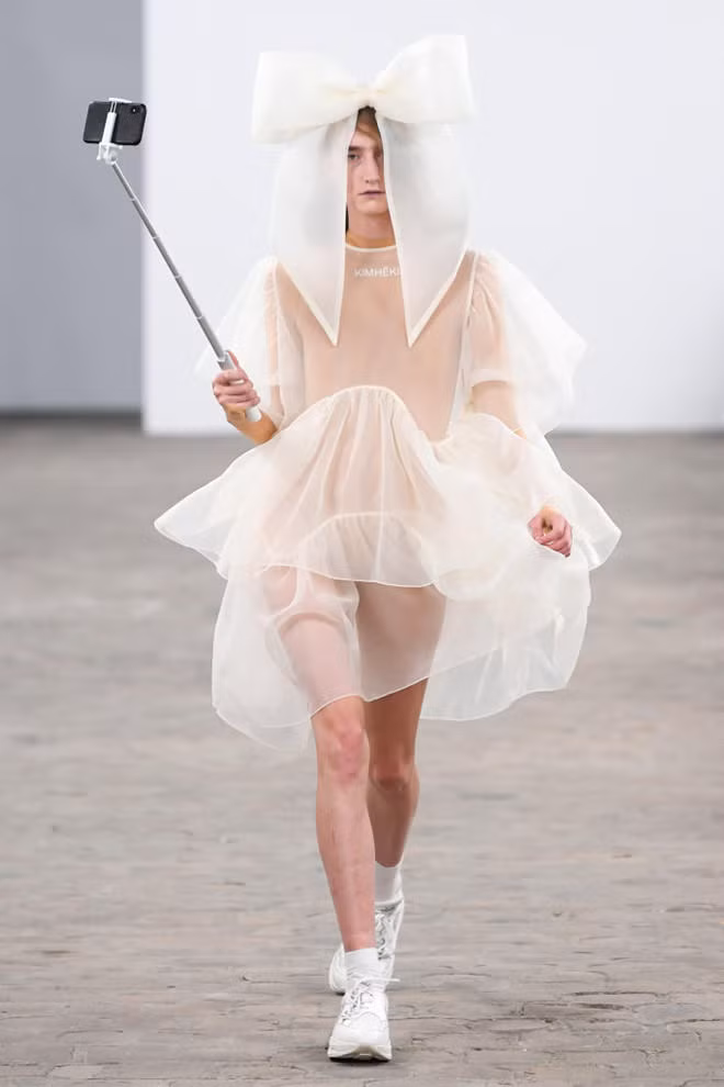 Người mẫu gây ấn tượng khi tay cầm gậy chụp ảnh và đội chiếc mũ hình chiếc nơ khổng lồ trên đầu.