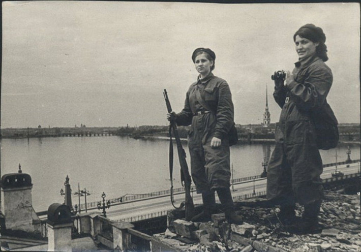 Trong khi đó, một số phụ nữ Liên Xô cầm súng và ống nhòm canh gác bầu trời Leningrad để kịp thời phát hiện máy bay Đức quốc xã.