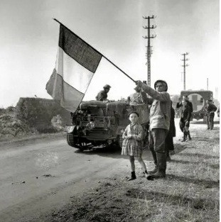 Hai ông cháu người Pháp vẫy cờ chào đón binh sĩ Canada khi hành quân tới Bretagne năm 1944.