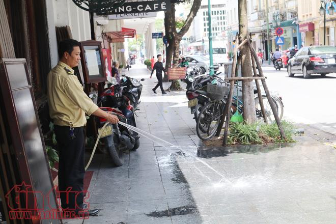 Bảo vệ của một cửa hàng phải phun nước giảm nhiệt độ để ngăn vỉa hè hắt nắng nóng lên.