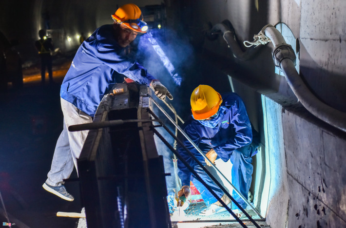 Bên trong công trình dài hun hút, nhiều nhóm công nhân chia làm các mũi lắp đặt lớp phòng nước đi trước, 5 mũi đổ bê tông vỏ hầm cần mẫn làm việc.