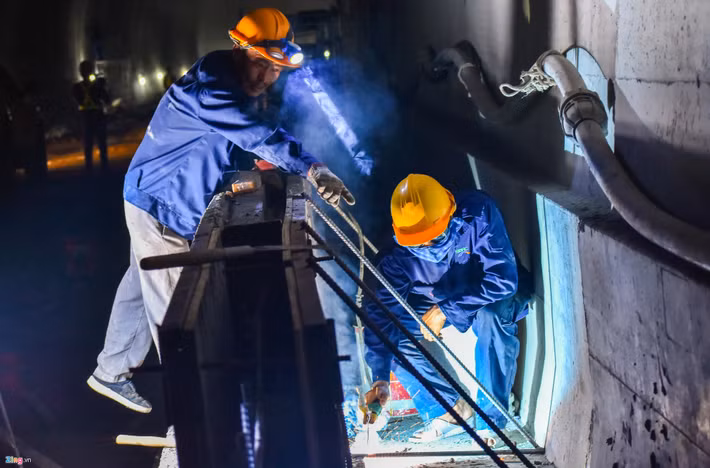 Bên trong công trình dài hun hút, nhiều nhóm công nhân chia làm các mũi lắp đặt lớp phòng nước đi trước, 5 mũi đổ bê tông vỏ hầm cần mẫn làm việc.