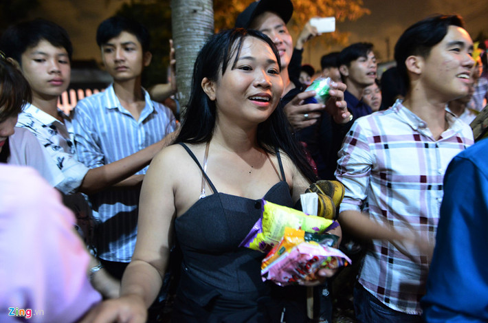 Cô gái ngụ huyện Châu Thành, Long An này phải kẹp dép bên nách cùng một số bánh trái thu được, đứng nhìn những người khác tranh giành bên trong.