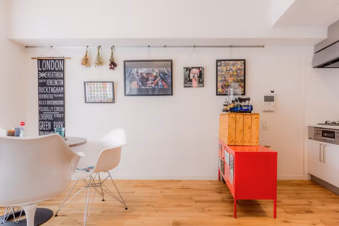 Chiếc bàn nhỏ nằm đối diện cửa sổ vừa là bàn ăn, vừa là nơi để để cả gia đình ngồi thư giãn, trò chuyện. Tivi được gắn trực tiếp lên bức tường để tiết kiệm diện tích. Trên tường còn treo thêm bức tranh chữ và vài khóm hoa khô xinh xắn. Một chiếc kệ tủ được đặt giữa khu bếp và phòng sinh hoạt chung, thay thế cho vách ngăn. Chiếc tủ sử dụng màu sơn đỏ, kết hợp với hộp gỗ mộc ở trên, trông có vẻ lạc điệu nhưng khi nhìn tổng thể lại tạo thành điểm nhấn độc đáo, thú vị.