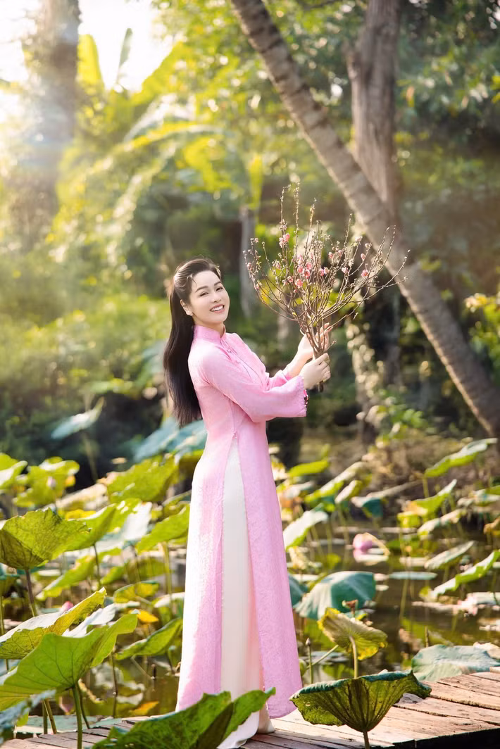 Nữ diễn viên – ca sĩ tạo dáng bên hồ sen, mai vàng và cành đào đỏ thắm để tăng sắc xuân cho bộ ảnh. Trên trang cá nhân, cô chia sẻ những câu thơ nhẹ nhàng, gửi gắm mong ước một năm mới an yên, nhiều niềm vui. “Áo hồng chạm nắng, xuân vừa kịp sang. Cười lên một cái, dịu dàng cả năm”, người đẹp viết trên trang cá nhân. Ảnh: FB Nhật Kim Anh.