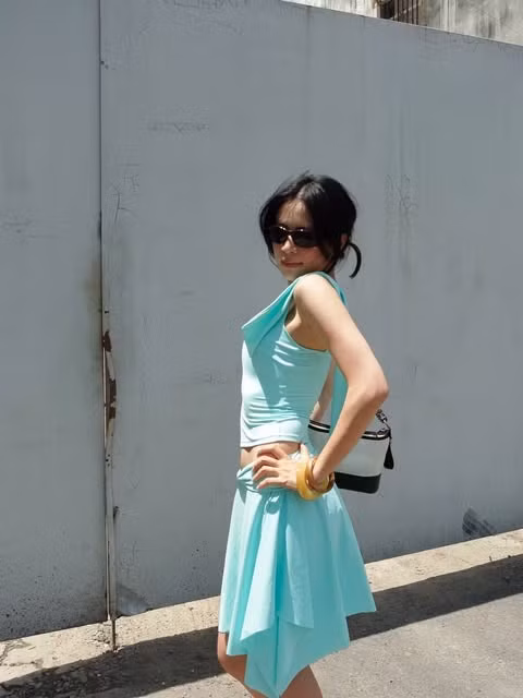 Ở một lần xuống phố khác, cô diện áo sát nách cùng chân váy bất đối xứng màu xanh ngọc. Kính râm đen, túi trắng - đen và vòng tay bản lớn phá vỡ cách phối đơn sắc, tạo vẻ cá tính hơn.