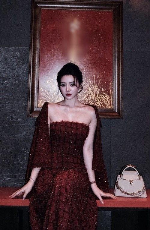 Cô diện váy hai dây màu đen, khoác ngoài áo choàng đỏ đính sequin lấp lánh, tạo điểm nhấn nổi bật trong khung hình tối.