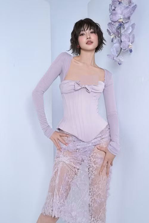 Nữ diễn viên diện áo corset ôm sát, tôn vòng eo và đường cong cơ thể, kết hợp chân váy ren xuyên thấu.