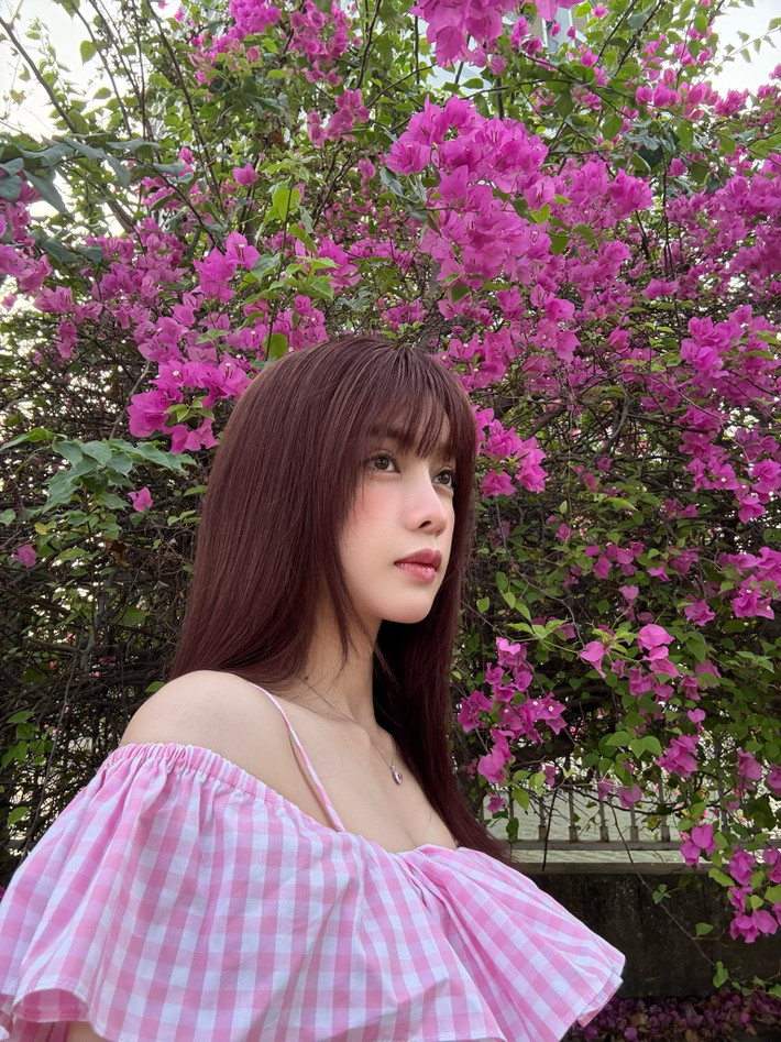 Chụp ảnh bên hoa, Trình Mỹ Duyên lựa chọn chiếc váy trễ vai họa tiết caro hồng – trắng, tôn lên bờ vai thon và xương quai xanh thanh mảnh.