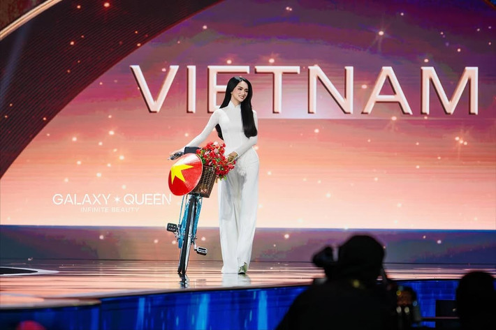 Trước đêm bán kết Miss Universe 2025, Hương Giang tham gia phần thi Trang phục dân tộc (National Costume). Đại diện Việt Nam diện áo dài trắng, dắt xe đạp trên sân khấu. Ảnh: Galaxy Queen.