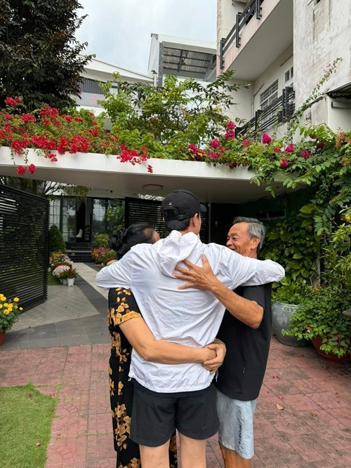 Trước cổng nhà phủ đầy hoa giấy đỏ rực, Quốc Trường dang tay ôm trọn bố mẹ vào lòng. Cái ôm chặt như muốn níu thêm vài phút ở lại bên gia đình.