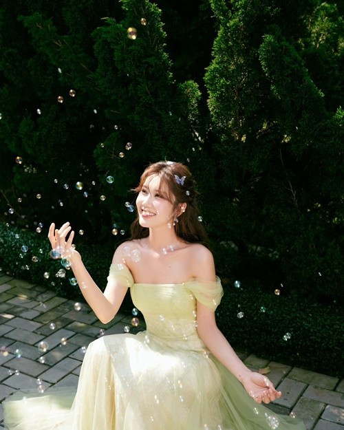 Nữ diễn viên diện chiếc váy dạ hội màu pastel với phần vai trễ, tôn bờ vai thanh mảnh. Khung cảnh ngoài trời cùng ánh sáng tự nhiên càng làm nổi bật nét trong trẻo của cô.