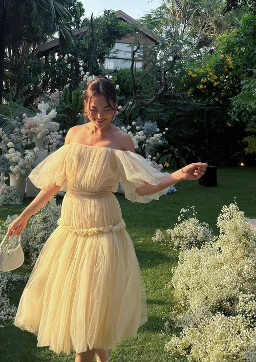 Khi diện váy voan trễ vai màu kem trong không gian vườn hoa, Thùy Anh toát lên vẻ dịu dàng, nữ tính. Thiết kế bồng nhẹ tạo cảm giác bay bổng, phù hợp với những bộ ảnh mang phong cách lãng mạn.