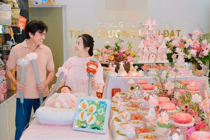 Bữa tiệc đầy tháng của bé Dâu Tây được vợ chồng Cao Minh Đạt chuẩn bị chỉn chu với không gian trang trí tông hồng chủ đạo, điểm xuyết hoa tươi và bánh kem tạo hình lâu đài cổ tích, mang đậm không khí ấm áp của một buổi sum họp gia đình.