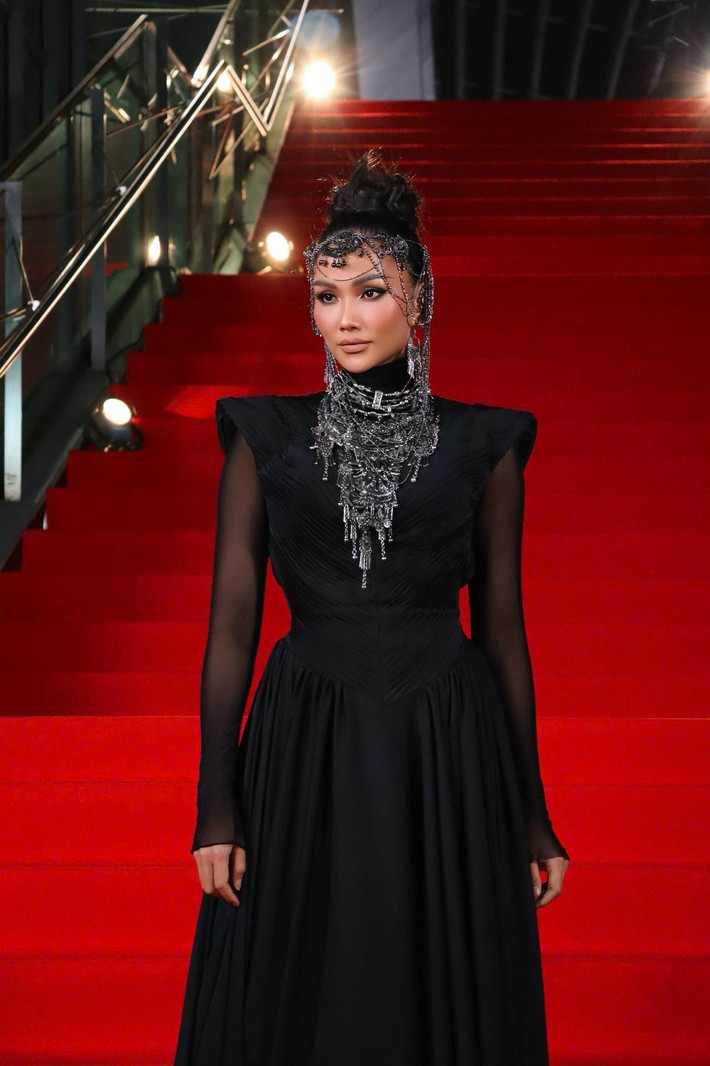 Điểm nhấn nổi bật của set đồ nằm ở bộ phụ kiện kim loại cầu kỳ phủ quanh cổ và trán, mang đến hiệu ứng thị giác mạnh mẽ, gợi liên tưởng đến vẻ đẹp huyền bí pha chút quyền lực. Tổng thể trang phục cho thấy sự tính toán kỹ lưỡng trong việc xây dựng hình ảnh: tối giản nhưng không đơn điệu.