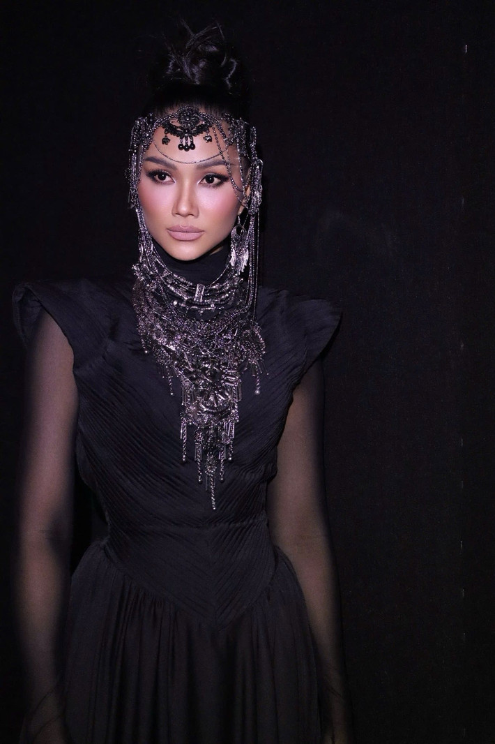 Trên thảm đỏ, H’hen Niê khoác lên mình bộ trang phục đen dáng dài, thiết kế ôm gọn phần thân trên với chi tiết vai dựng sắc nét kết hợp tay áo xuyên thấu, tạo cảm giác vừa cá tính vừa bí ẩn. Phần chân váy rủ mềm, chuyển động uyển chuyển theo từng bước đi, giúp tôn lên vóc dáng săn chắc và cân đối.