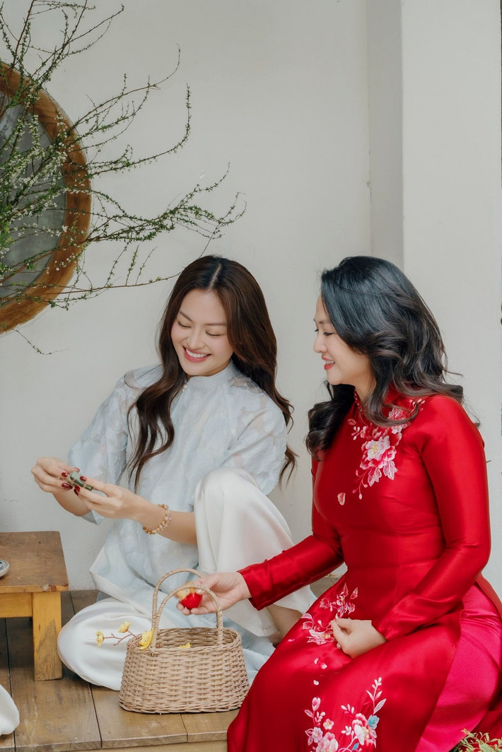 Trong khung hình, mẹ của Thùy Anh nổi bật với tà áo dài đỏ rực, chất liệu bóng nhẹ, được thêu hoa tinh xảo dọc thân áo. Mái tóc đen uốn sóng mềm mại cùng gương mặt rạng rỡ, phúc hậu giúp bà ghi điểm.