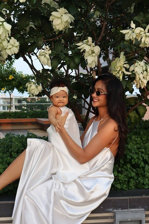 Trong những khoảnh khắc đời thường bên con, H’Hen Niê chuộng phong cách tối giản: khi là chiếc váy lụa trắng giữa khu vườn xanh mát, lúc lại diện bộ đồ hồng rực rỡ và ôm con trong vòng tay. Ảnh: FB H’Hen Niê.