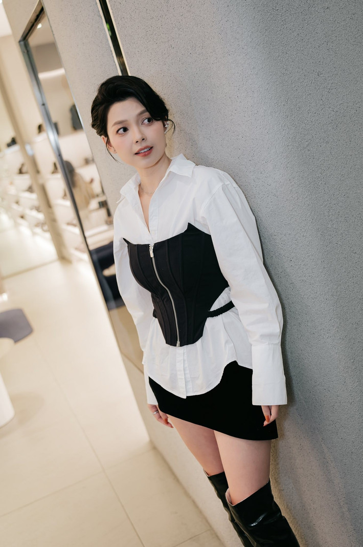 Tham gia một sự kiện, người đẹp lựa chọn sơ mi trắng dáng rộng kết hợp corset đen ôm sát, tạo điểm nhấn rõ nét cho vòng eo và mang hơi hướng thời trang cao cấp, thời thượng. Chân váy ngắn cùng boots cao cổ giúp tổng thể thêm phần năng động, gợi cảm và mạnh mẽ, đồng thời tôn lên đôi chân thon gọn.