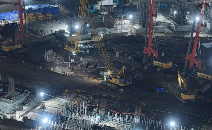 Những đêm cuối tháng 4, khu vực công trường Sân vận động Hùng Vương rực sáng ánh đèn. Hàng nghìn công nhân, máy móc hoạt động liên tục, xe tải ra vào không ngừng nghỉ, tạo nên nhịp thi công khẩn trương hiếm thấy tại một dự án thể thao ở Việt Nam.