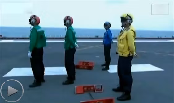 Các thủy thủ tàu sân bay Liêu ninh Trung Quốc đội mũ bảo hiểm, mặc quần áo màu xanh dương, xanh lá cây và vàng chuẩn bị làm nhiệm vụ chỉ hướng cho chiến đấu cơ J-15.
