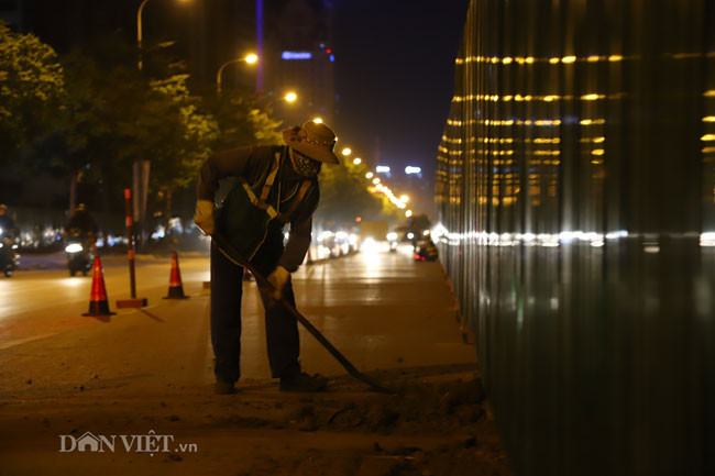 Một công nhân luôn túc trực quét dọn phần đất vương vãi trên mặt đường. Ảnh chụp tại đoạn đang thi công trên đoạn đường Khuất Duy Tiến - Phạm Hùng.