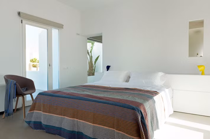 Phòng ngủ sáng trắng, với điểm nhấn chính là bộ ga giường kẻ sọc nhiều màu sắc.