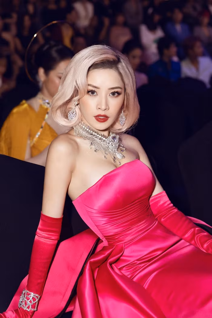 Chi Pu mặc nguyên bộ đầm lụa màu hồng. Đây được xem là gam màu kén chọn người mặc. Khá “cao tay”, dù chọn nhiều phụ kiện như vòng cổ, vòng tay, khuyên tai to bản đi kèm song người đẹp rất biết tiết chế khi chọn trang sức màu ánh kim. Thậm chí, cô cũng nhuộm tóc màu trung tính để tiết chế màu sắc.