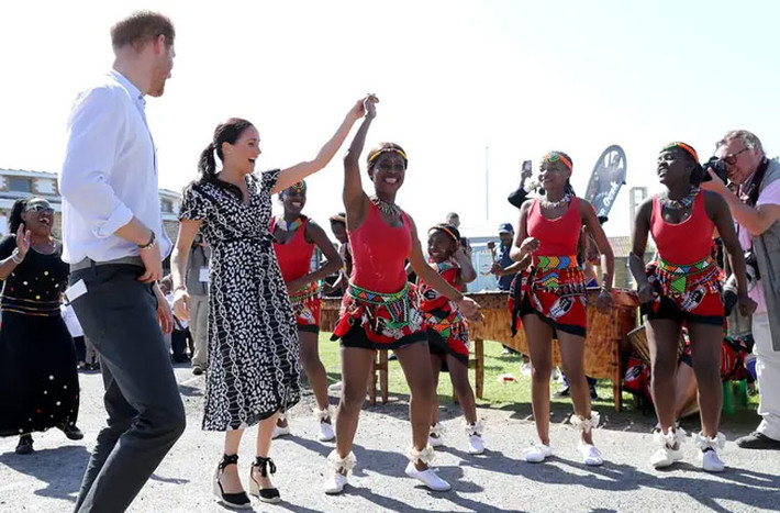 Tháng 9/2019: Meghan và Harry bắt đầu chuyến công tác ở Châu Phi. Ảnh: Harry đứng nhìn vợ vui vẻ nhảy múa với người dân địa phương trên đường phố Châu Phi.