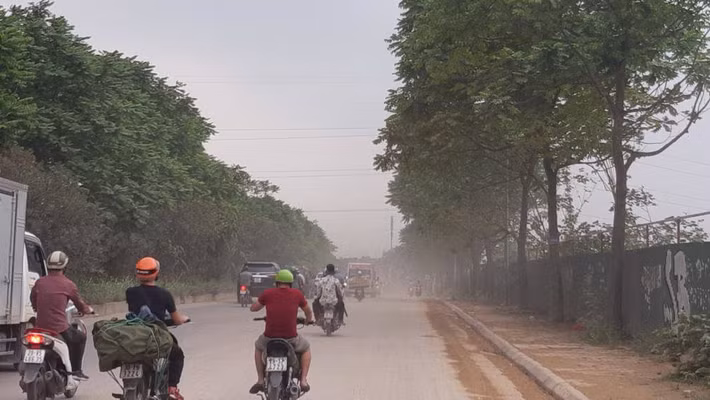 Trên tuyến đường thường xuyên xuất hiện xe tải hạng nặng lưu thông qua không che chắn theo quy định gây bụi bẩn. Trong ảnh người đi đường phải di chuyển chậm lại, tay bịt mũi để ngăn bụi