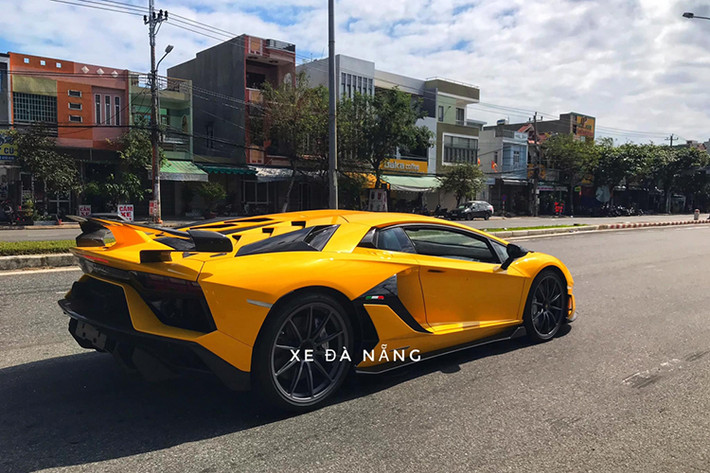 Ngoài màu sơn váng óng, chiếc siêu xe Lamborghini Aventador SVJ tại Việt Nam còn có nhiều chi tiết carbon ở cản va trước và cản va sau, ốp sườn, hốc gió bên hông hay nổi bật nhất vẫn là cánh gió đuôi carbon với điểm nhấn là hệ thống chủ động Aerodinamica Lamborghini Attiva (Ala 2.0) mới nhất của hãng xe Ý.