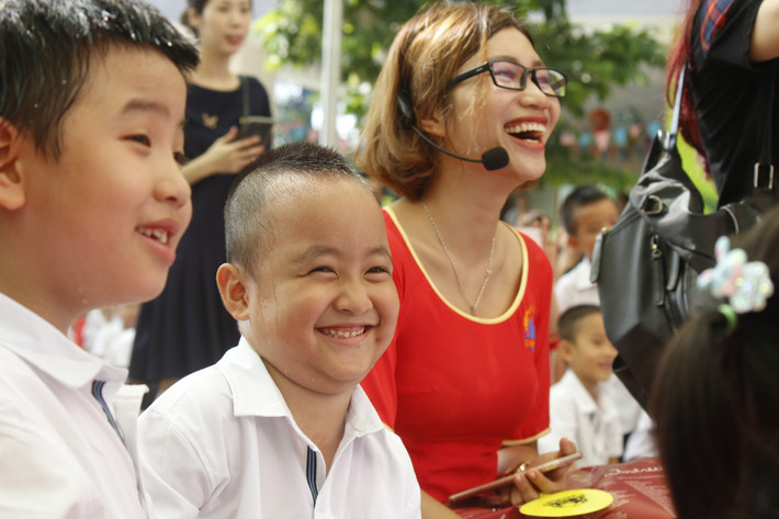 Cậu học trò cười tươi cùng bạn bè và cô giáo.