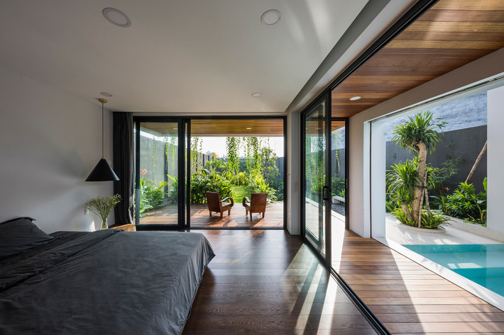 Phòng ngủ với lớp cửa kính lớn, nhìn ra bể bơi và sân chính.