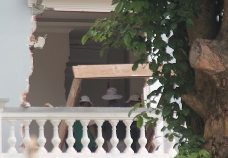 Khung gỗ đặt ngay trên thành lan can, bên trong, các công nhân đang tháo dỡ thêm các phần khác của ngôi nhà. Ảnh: Lê Phi