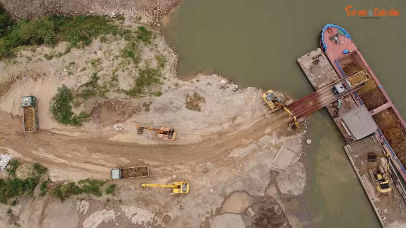 Xe tải nhộn nhịp vào bãi vật liệu trong đất dự án để đổ đất xuống sà lan.