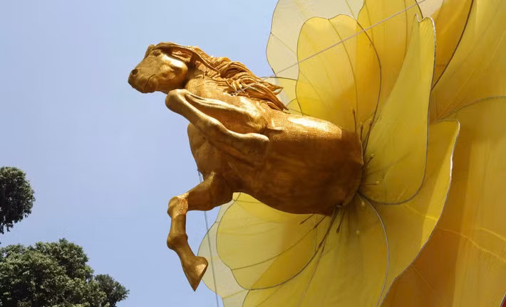 Du khách bị thu hút bởi hình ảnh một chú ngựa vàng dũng mãnh đang phi nước đại, vươn mình ra từ tâm của một đóa hoa mai khổng lồ rực rỡ.