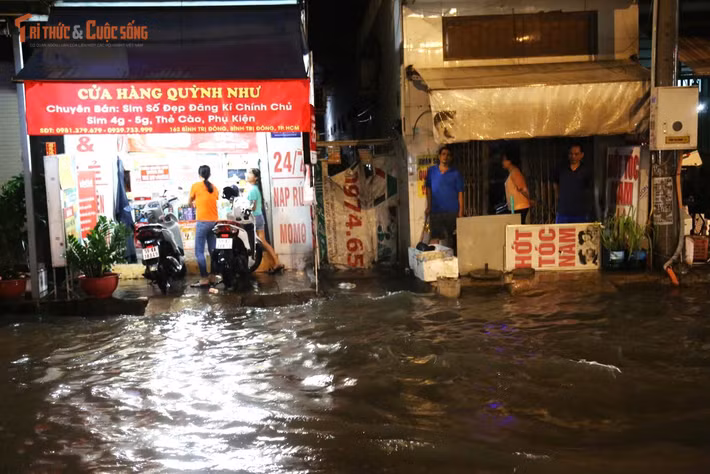 Nước ngập tràn vào trước cửa nhiều cửa hàng, quán ăn dọc đường Bình Trị Đông khiến hoạt động kinh doanh bị đình trệ. Nhiều người dân phải kê cao hàng hóa để tránh bị hư hỏng.
