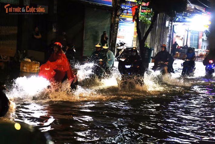 Dòng xe nối đuôi nhau di chuyển chậm chạp giữa biển nước trên đường Bình Trị Đông. Người lớn vất vả điều khiển xe, trẻ nhỏ mệt mỏi ngồi sau yên. Người đi bộ phải men sát nhà dân để tránh các hố ga bị nước che khuất.
