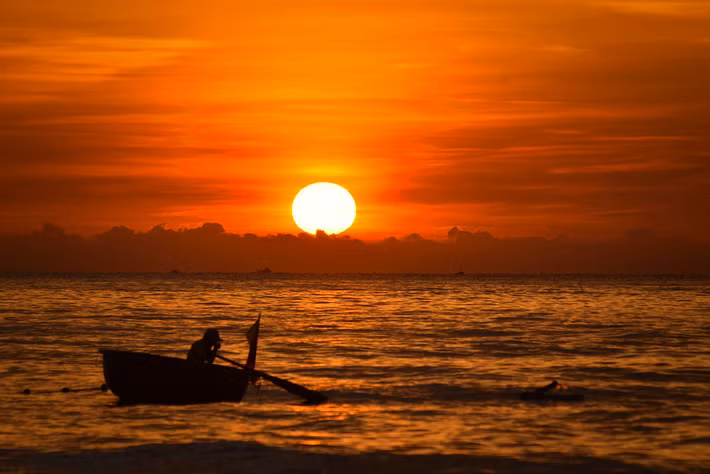 Con thuyền thúng nhỏ bé dưới vầng mặt trời đỏ rực. Ảnh: Raita Futo/ Flickr.