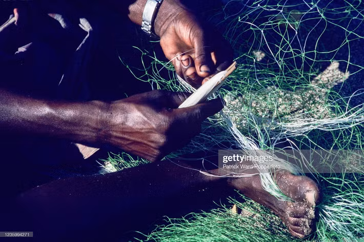 Một người ngư dân vá lại tấm lưới đánh cá.
