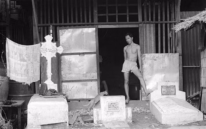 Người thanh niên và chú mèo đứng trước ngôi nhà lụp xụp của mình ở khu Mả Lạng, những ngôi mộ choán ngay cửa nhà, Sài Gòn 1968. Khu dân cư này được bao quanh bởi bốn con đường Võ Tánh (Ngyễn Trãi), Cống Quỳnh, Nguyễn Cư Trinh và Phát Diệm (Trần Đình Xu).