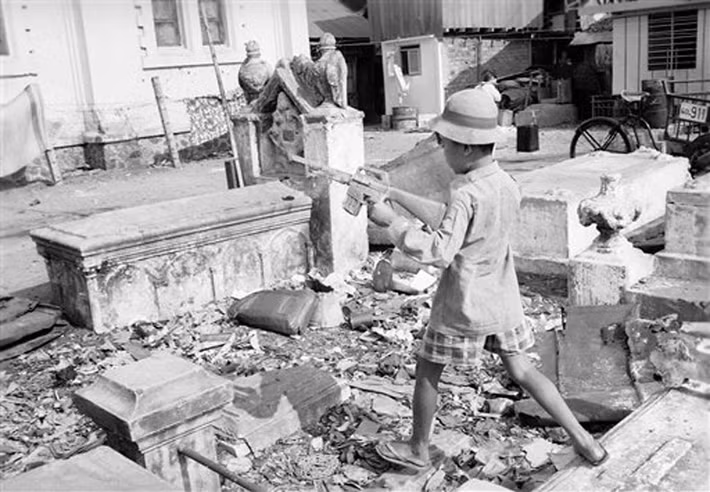 Trẻ ẻm chơi đùa với súng nhựa ở khu nghĩa địa không có người chăm nom, tràn ngập rác. Mả Lạng vốn là một nghĩa trang Công giáo có từ thời Pháp thuộc, bị bỏ hoang từ năm 1954. Người nghèo và dân tỵ nạn chiến tranh đã về đây cư ngụ, tạo nên một khu ổ chuột giữa trung tâm Sài Gòn.