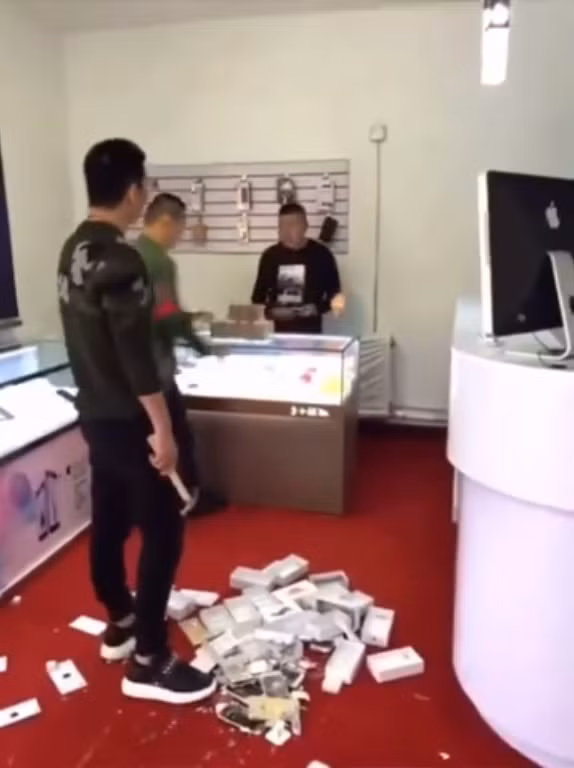 Để thể hiện độ giàu có, chàng thanh niên Trung Quốc chồng tiền mua 10 chiếc iPhone rồi đập nát. Ảnh: Youtube.