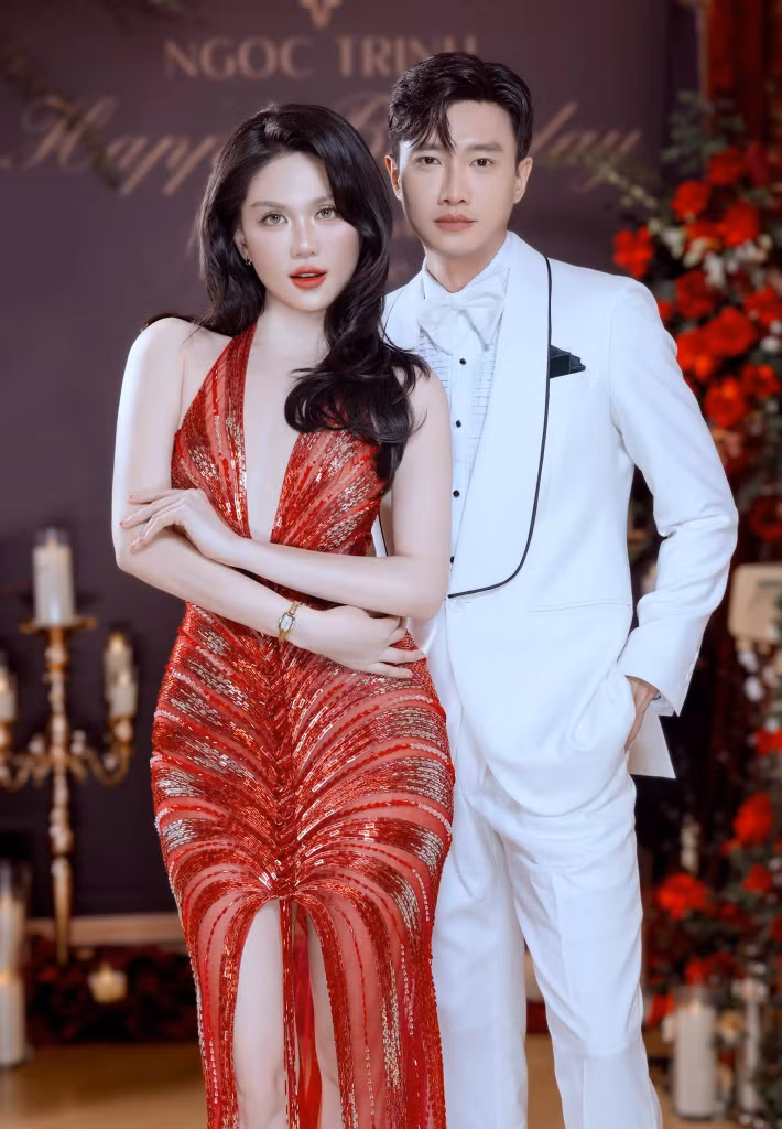 Trong loạt ảnh được chia sẻ, Ngọc Trinh diện váy đỏ đính kết, đứng cạnh Quốc Trường trong bộ suit trắng. Hai người cùng tạo dáng tại không gian tiệc được trang trí với hoa đỏ và ánh nến. Ảnh: FB Quốc Trường.
