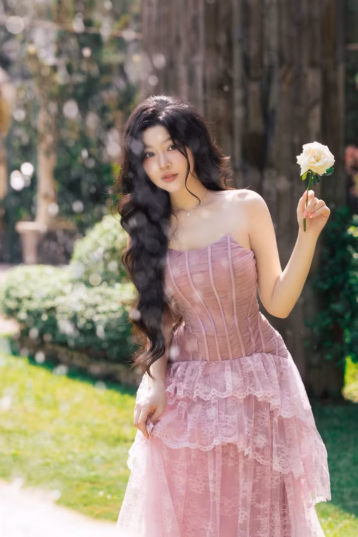 Lọ Lem chọn váy quây hồng với thân corset ôm dáng và chân váy ren xếp tầng. Thiết kế làm nổi bật bờ vai và vóc dáng mảnh mai. Tóc dài uốn sóng, trang điểm tông hồng đồng điệu với trang phục, tạo hình ảnh ngọt ngào hơn. (Ảnh: FB Mai Thảo Linh)