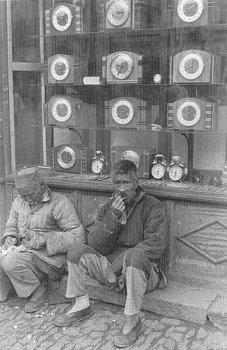 Hai người đàn ông lớn tuổi ngồi trước cửa hàng đồng hồ.