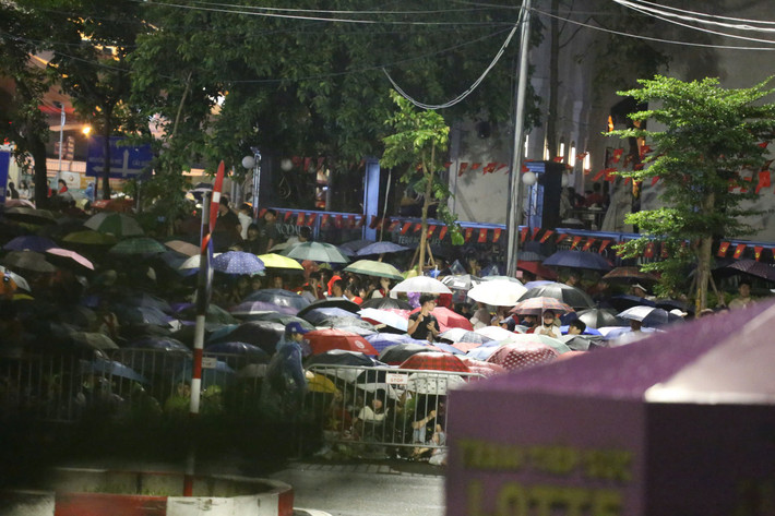 Mọi người che ô, mặc áo mưa yên vị, xếp hàng chờ đợi.