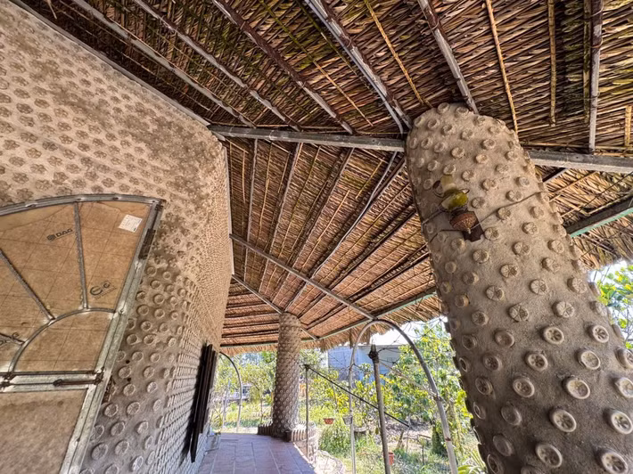 Từ cổng chính rẽ trái, men theo lối đi rợp bóng cây, ngôi đền dần hiện ra như một điểm nhấn giữa thiên nhiên. Không cầu kỳ, công trình được lợp mái lá đơn sơ, xung quanh là những tán cây xanh mát, mang lại cảm giác gần gũi, hài hòa.